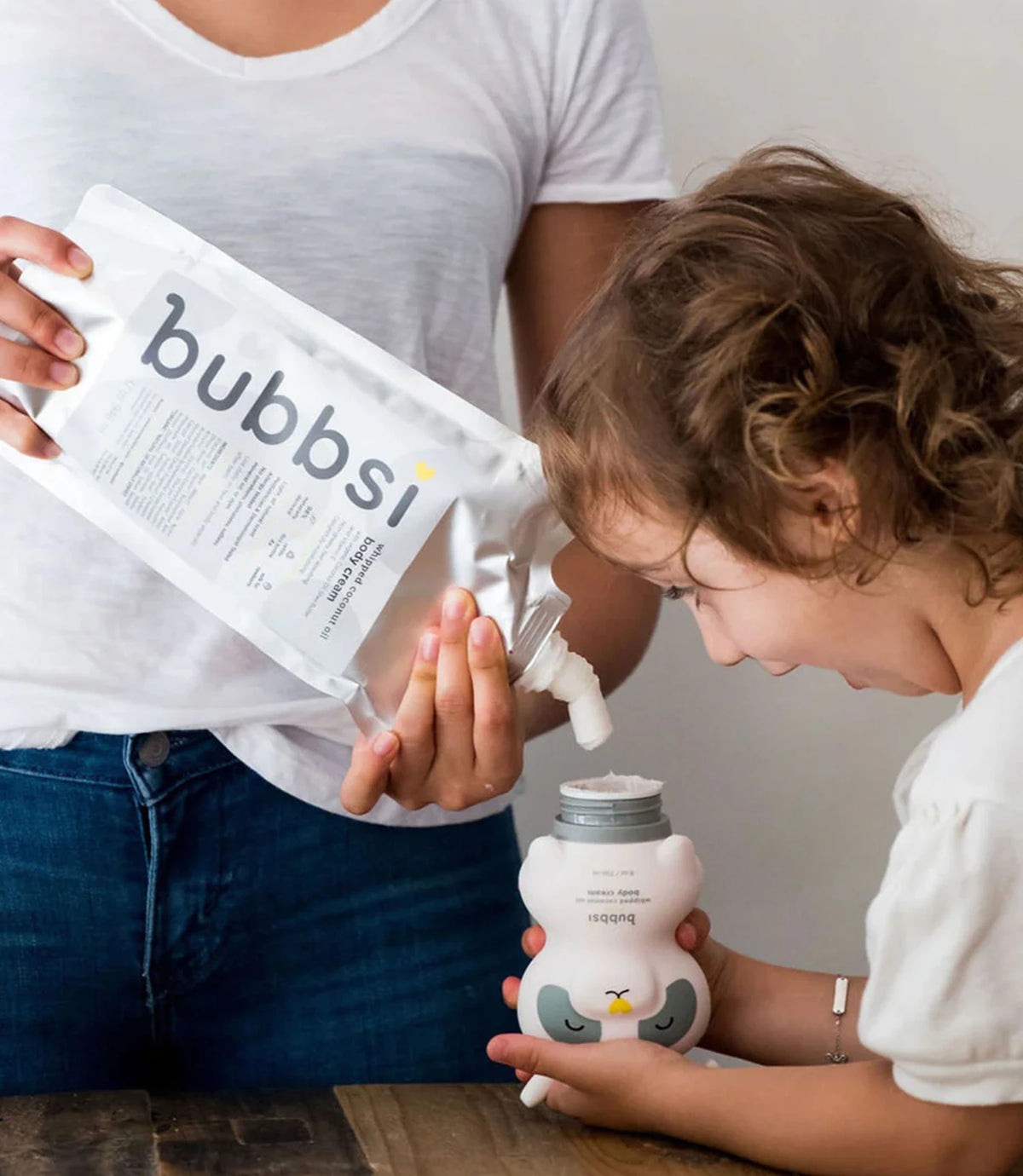 Parent helping child refill a Bubbsi body cream bottle