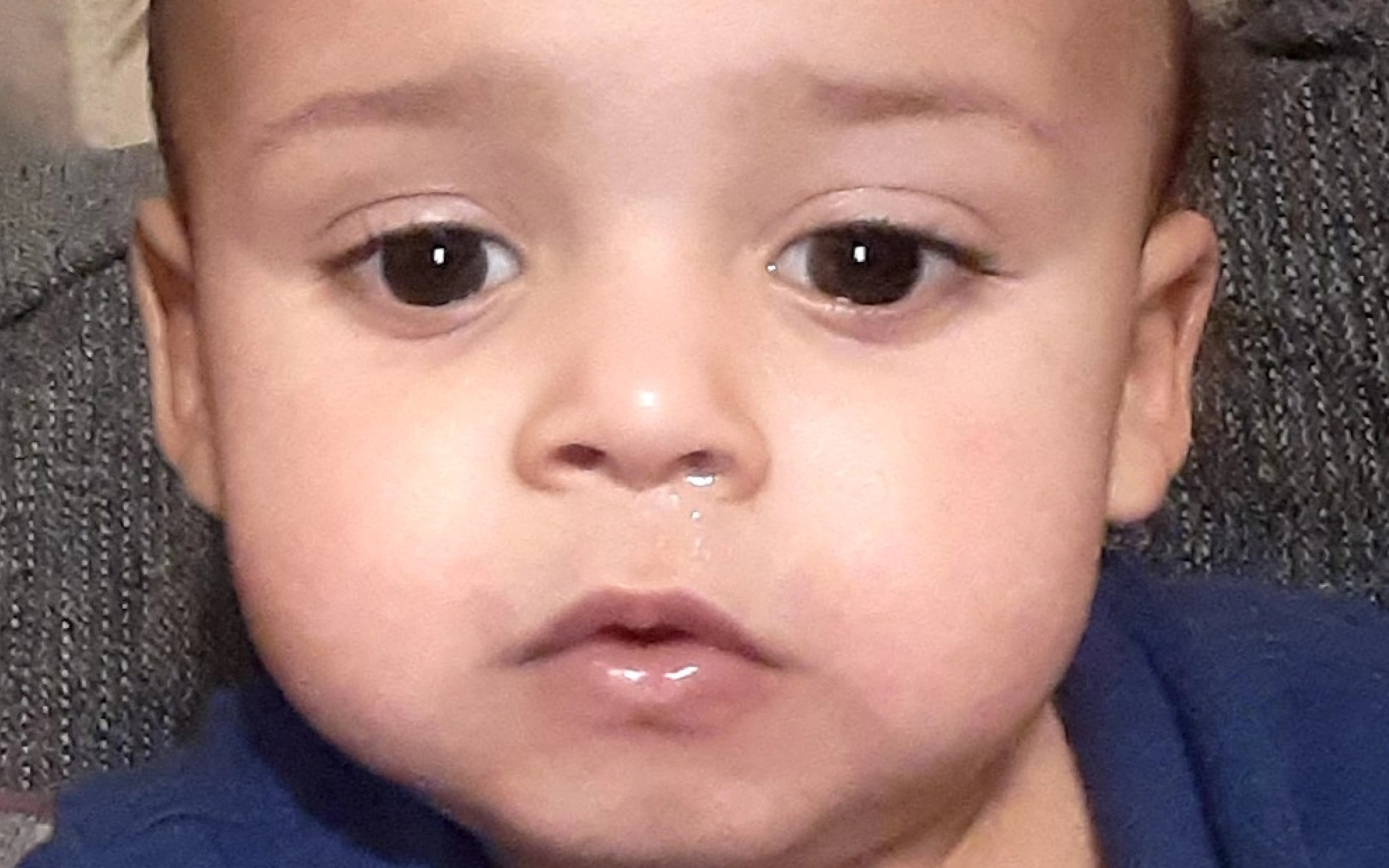 Close-up of a baby with healed eczema cheeks wearing a blue shirt against a neutral background